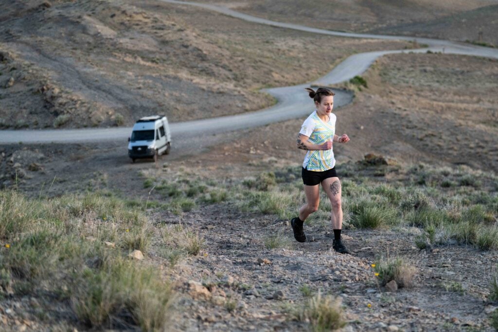 woman running up dirt hill with camper van in distance