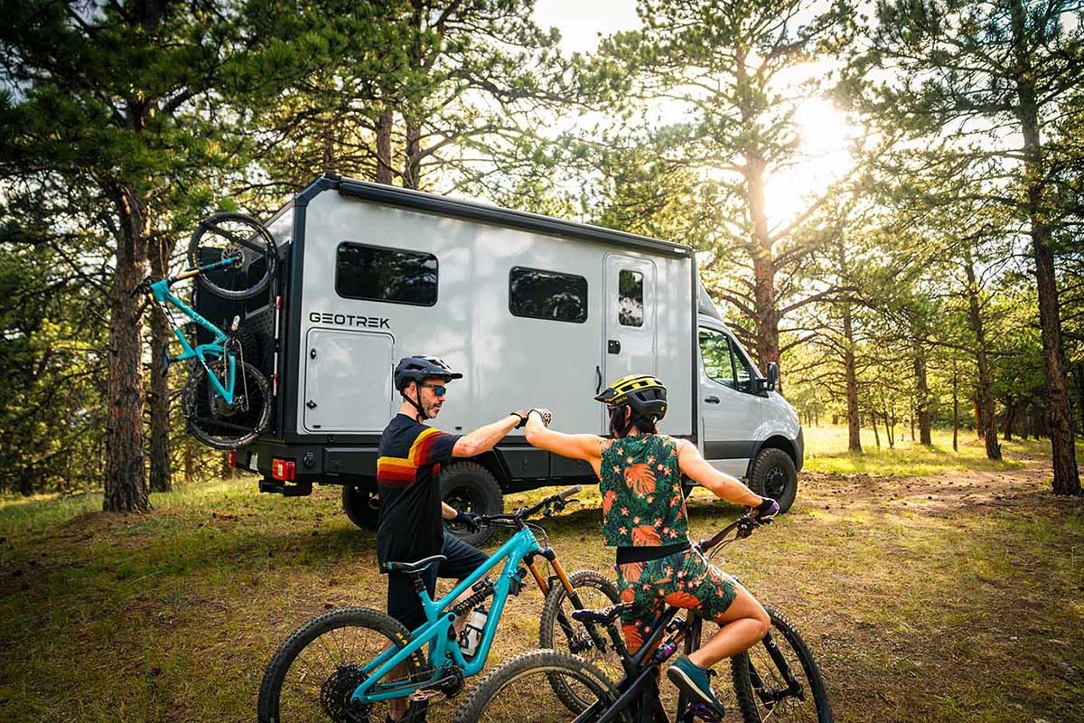 Couple on mountain bikes in front of a Geotrek Verus with a third bike on the rear rack