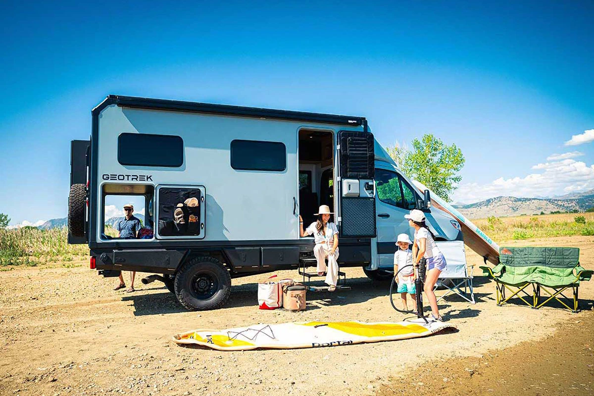 Family unloading stand-up paddleboards from the open rear garage of a Geotrek Verus