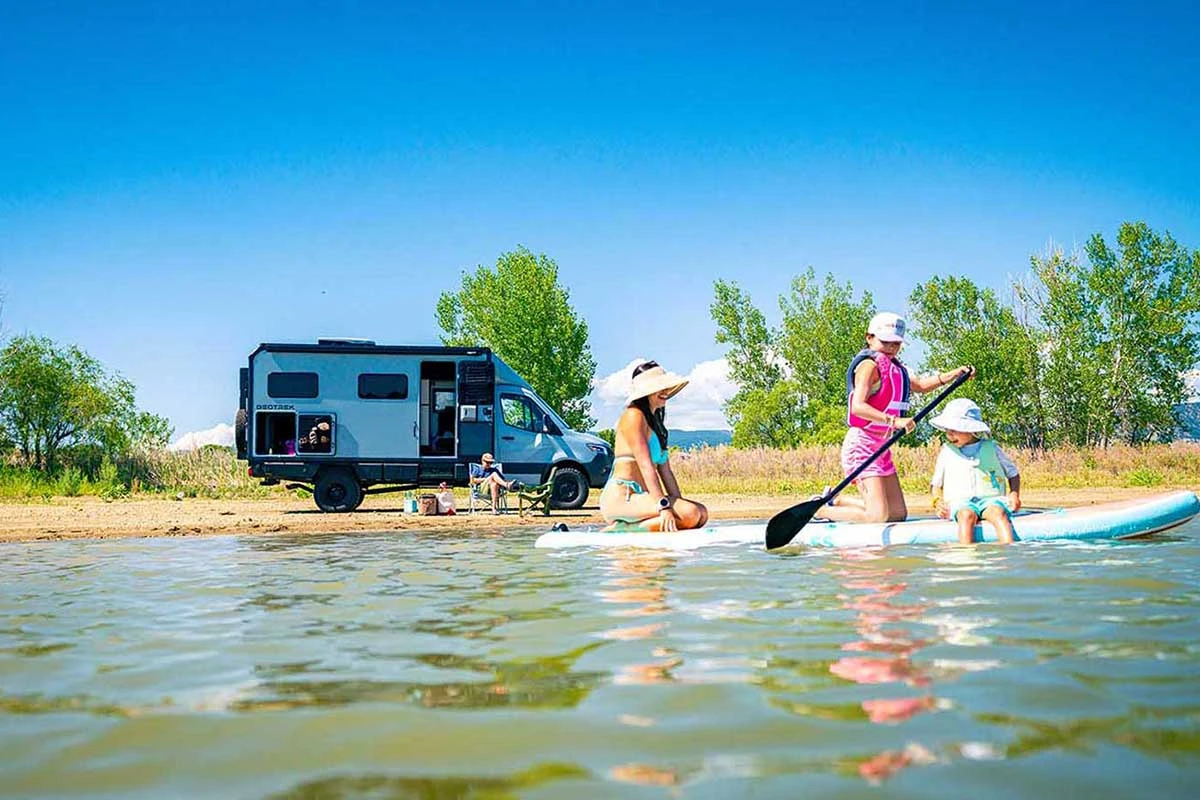 Family paddleboarding on a lake with a Geotrek Verus parked on the beach behind them