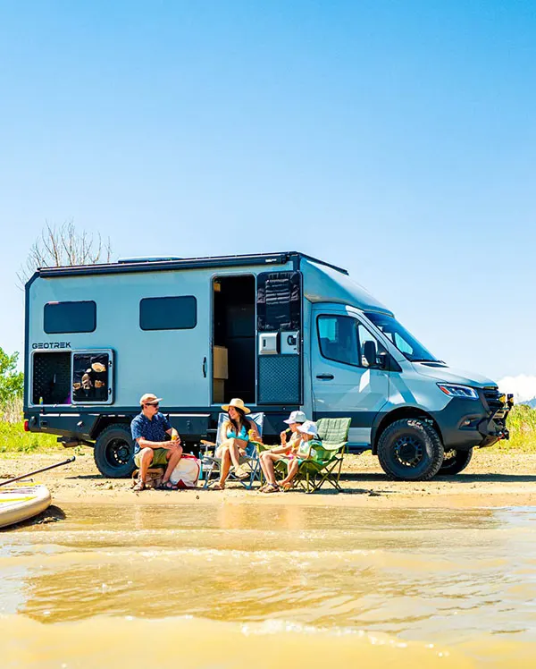 Two adults and two kids in camping chairs on a sandy beach in front of a Geotrek Verus